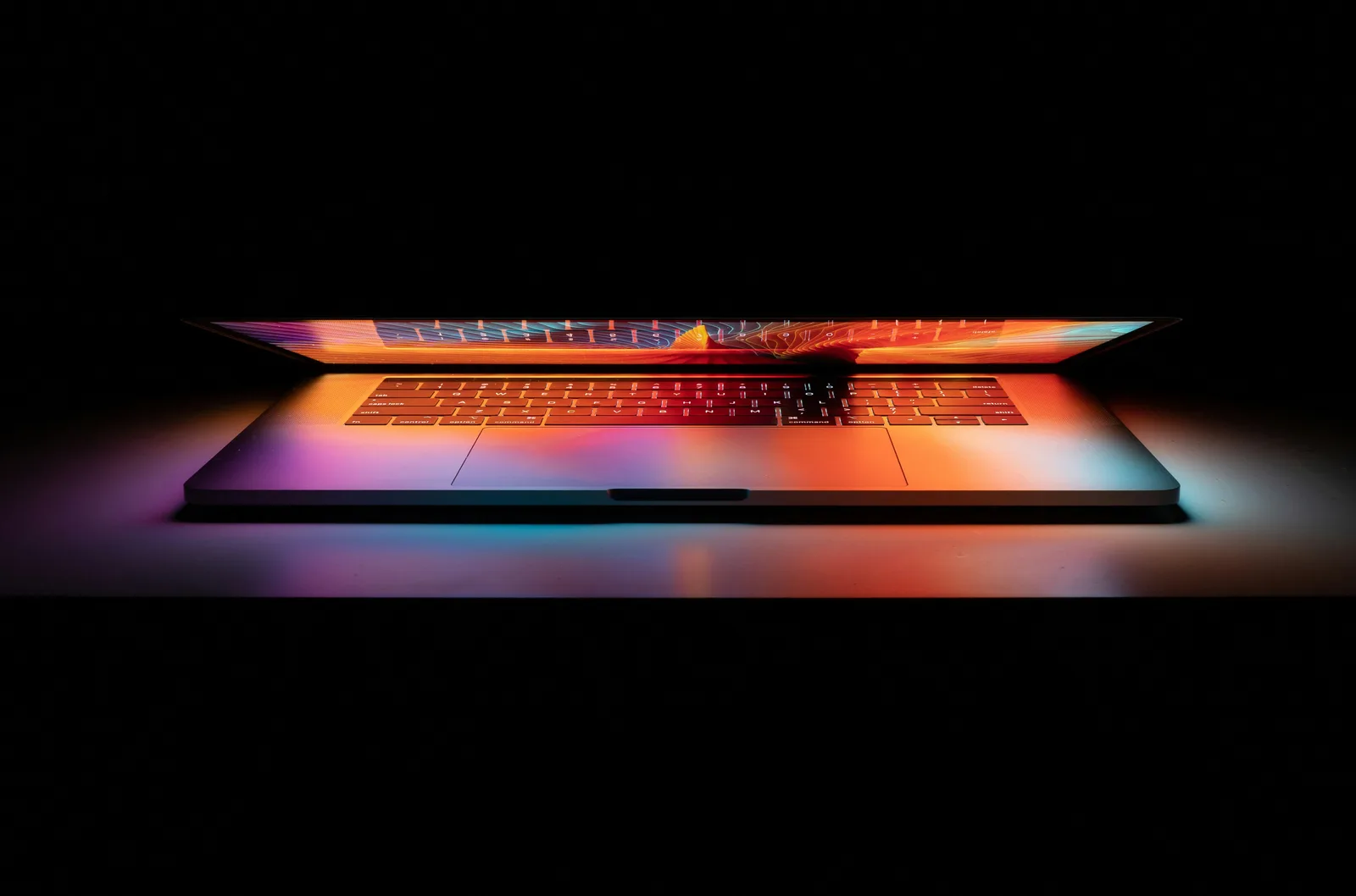 A partially open laptop glowing with colourful light, symbolising AI SEO optimisation and the technology behind improving content visibility across AI search engines like ChatGPT and Gemini.