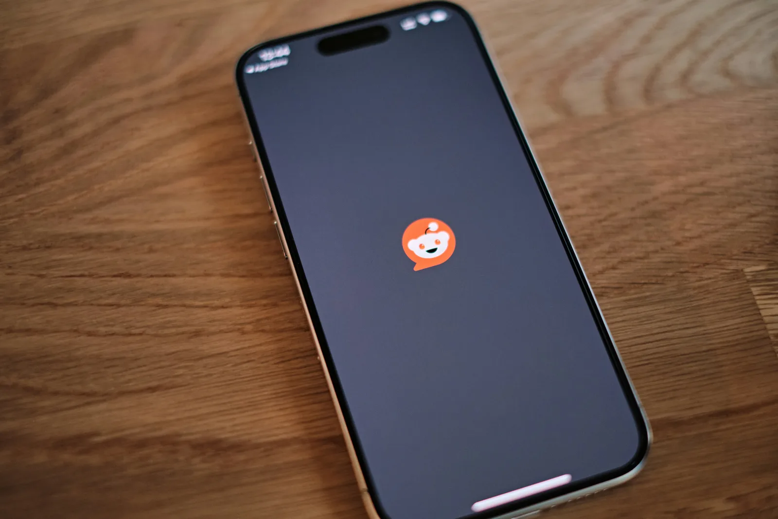 A smartphone displaying the Reddit app loading screen on a wooden surface, representing online community engagement and digital conversations.