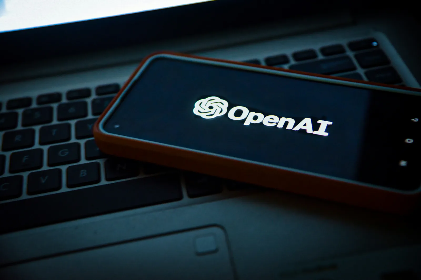 Smartphone displaying the OpenAI logo placed on a laptop keyboard, symbolizing AI technology integration.
