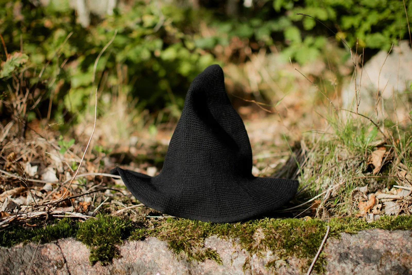 A black, pointed witch hat resting on moss-covered ground in a forest setting.
